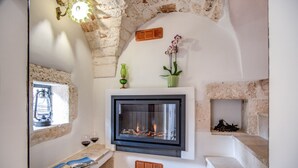 A fireplace with a stone wall, a window with a view, and a small shelf with a vase and a book. - Palazzo Stunis- Dimora di Charme (Ostuni)