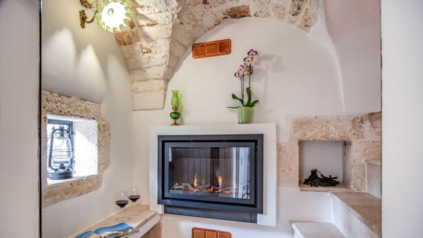 Una chimenea con pared de piedra, una ventana con vistas y un estante pequeño con un jarrón y un libro.