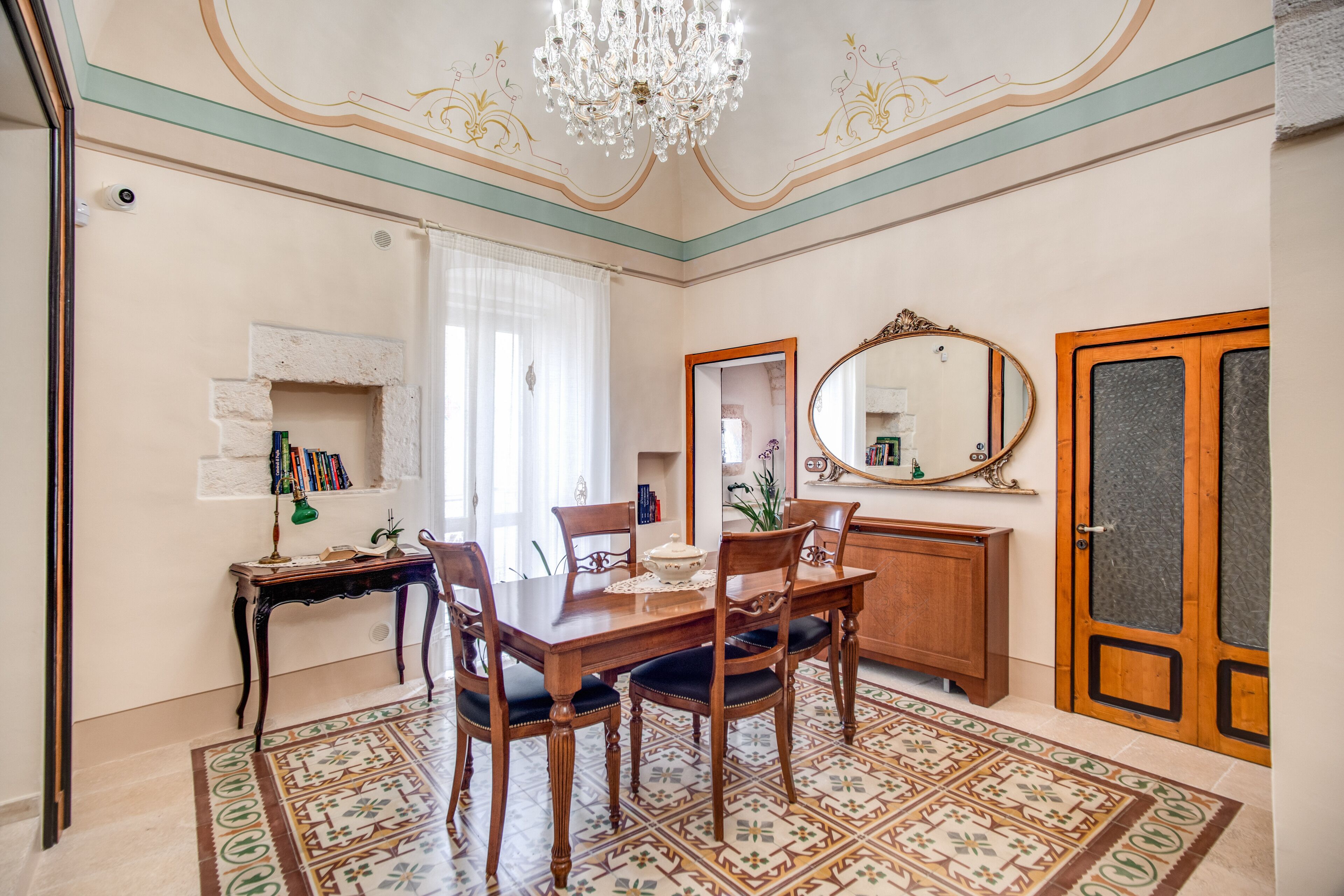 Un comedor con una mesa de madera, sillas, una araña y baldosas de suelo estampadas.