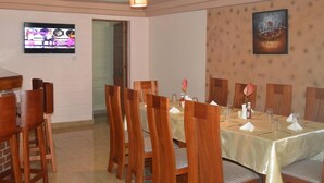 Un comedor con sillas y mesas de madera, un televisor en la pared y un cuadro colgado.