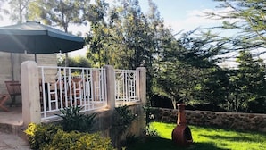 Un patio con cerca blanca, mobiliario exterior y pared de piedra.