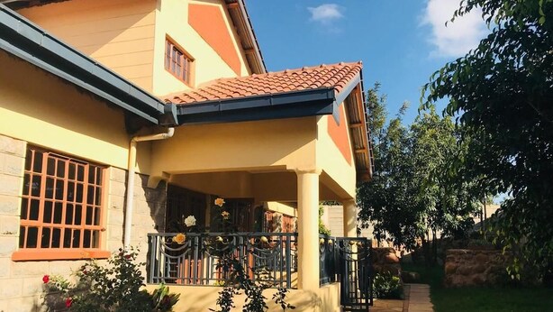 Una casa con porche cubierto, fachada de piedra y jardín con diversas plantas y flores.