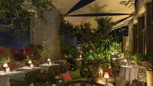 Un área de comedor al aire libre con mesas y sillas, rodeada de plantas y flores en macetas.