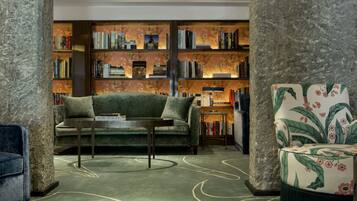 Un salón acogedor con un sofá verde, un sillón estampado y una estantería llena de libros.