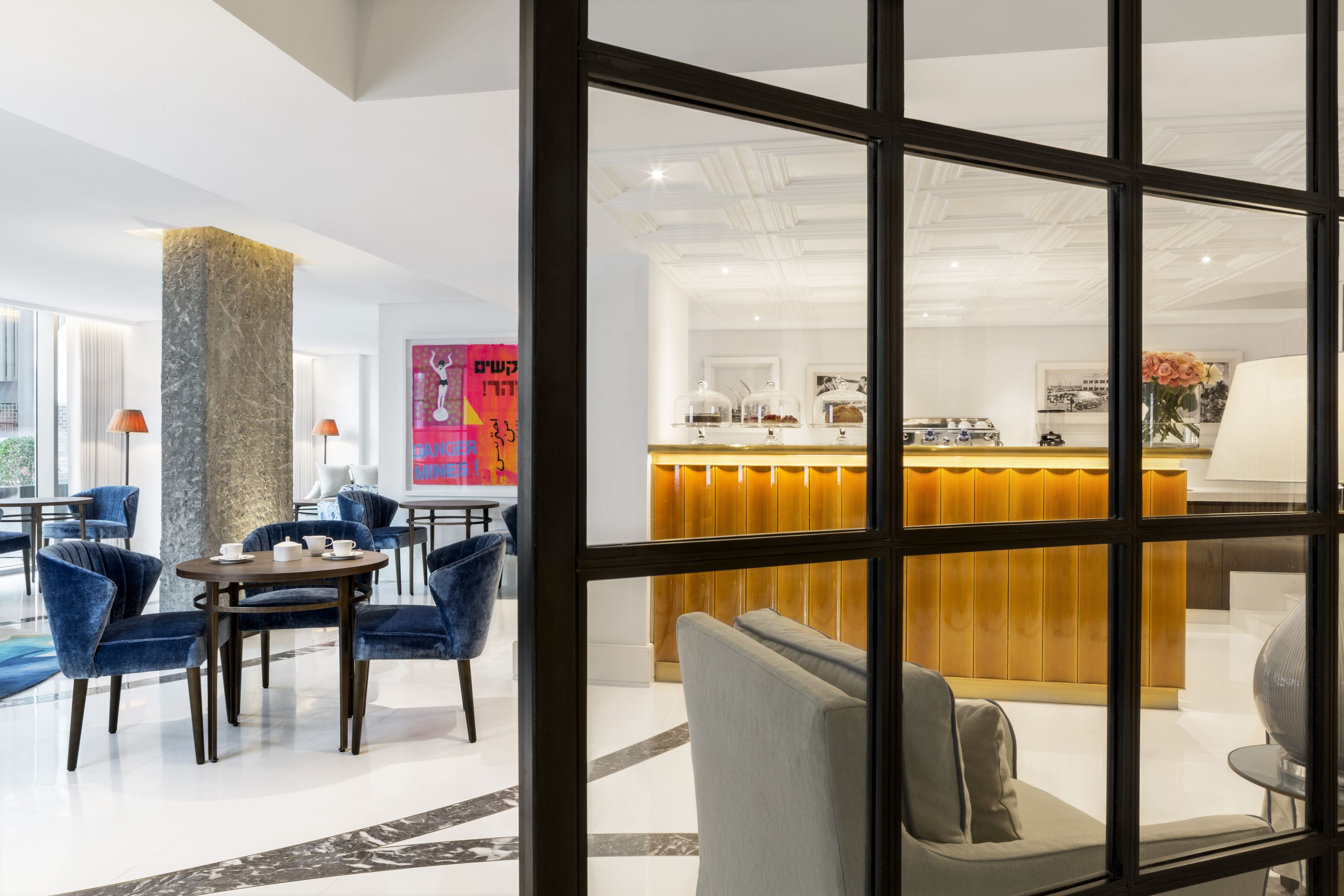 A modern hotel lobby with a seating area, a reception desk, and a view through a glass partition.