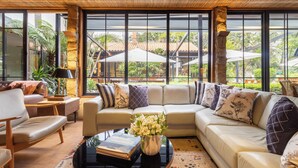 A modern living room with a large sectional sofa, a coffee table, and a view of a tropical garden through large windows.