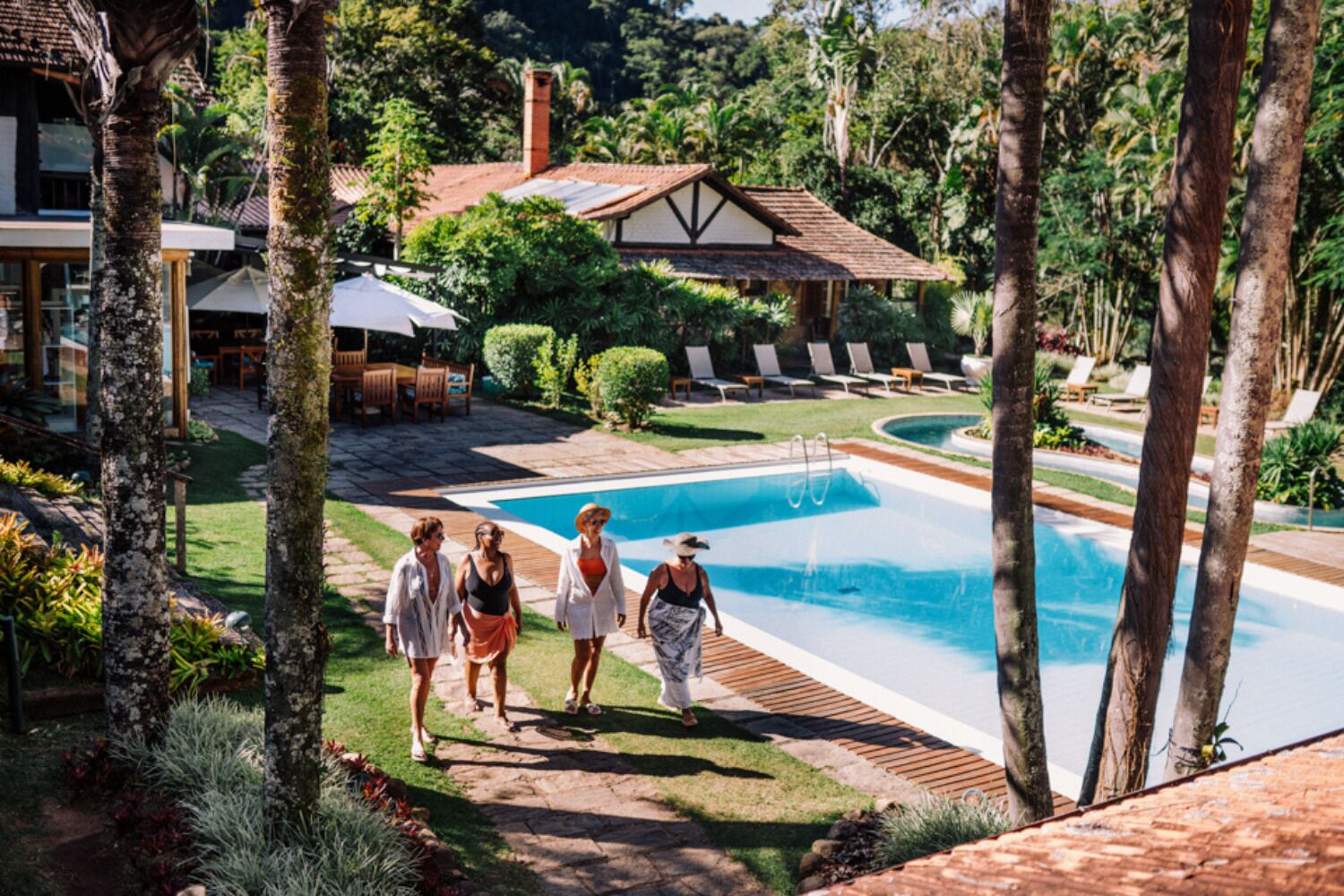 Uma área de piscina com vista clara da piscina, cadeiras de lounge e um edifício com telhado em azulejos.