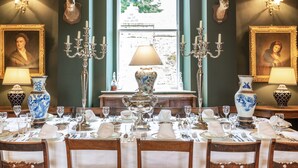 A formal dining room with a table set for a meal, two chandeliers, and framed deer heads on the walls. - Wardhill Castle (Inverurie)