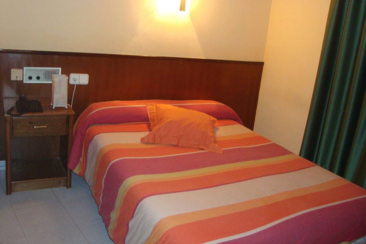 Ein Hotelzimmer mit Bett, Nachttisch, Lampe und einer Steckdose.
