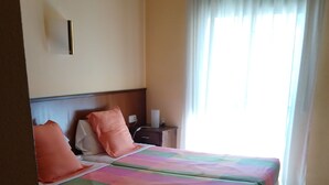 A hotel room with a bed, a nightstand, a lamp, and a window with curtains. - Hostal Les Collades (Sort)