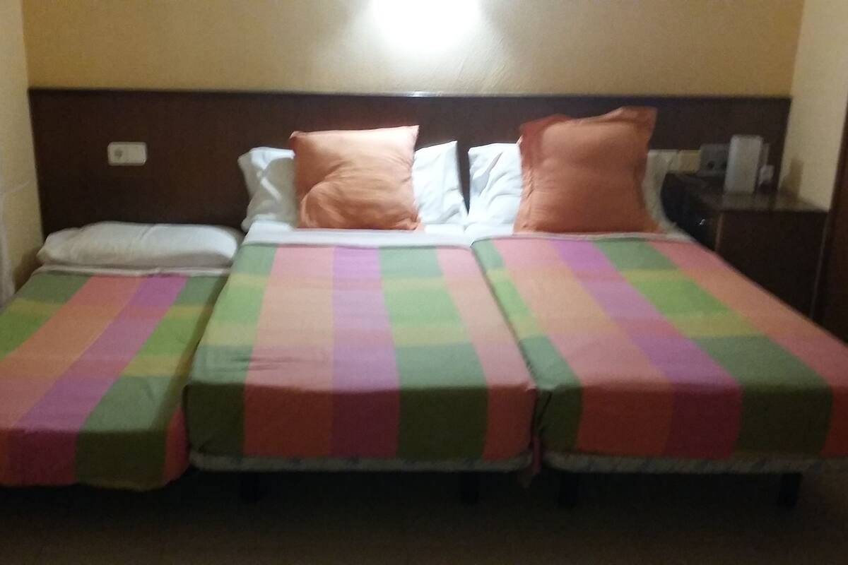 Ein Hotelzimmer mit zwei Einzelbetten, jeweils mit einer farbenfrohen, gestreiften Bettdecke.