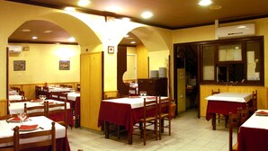 A restaurant with multiple tables, each covered with a red tablecloth and white tablecloths, wooden chairs, and a tiled floor. - Hostal Les Collades (Sort)