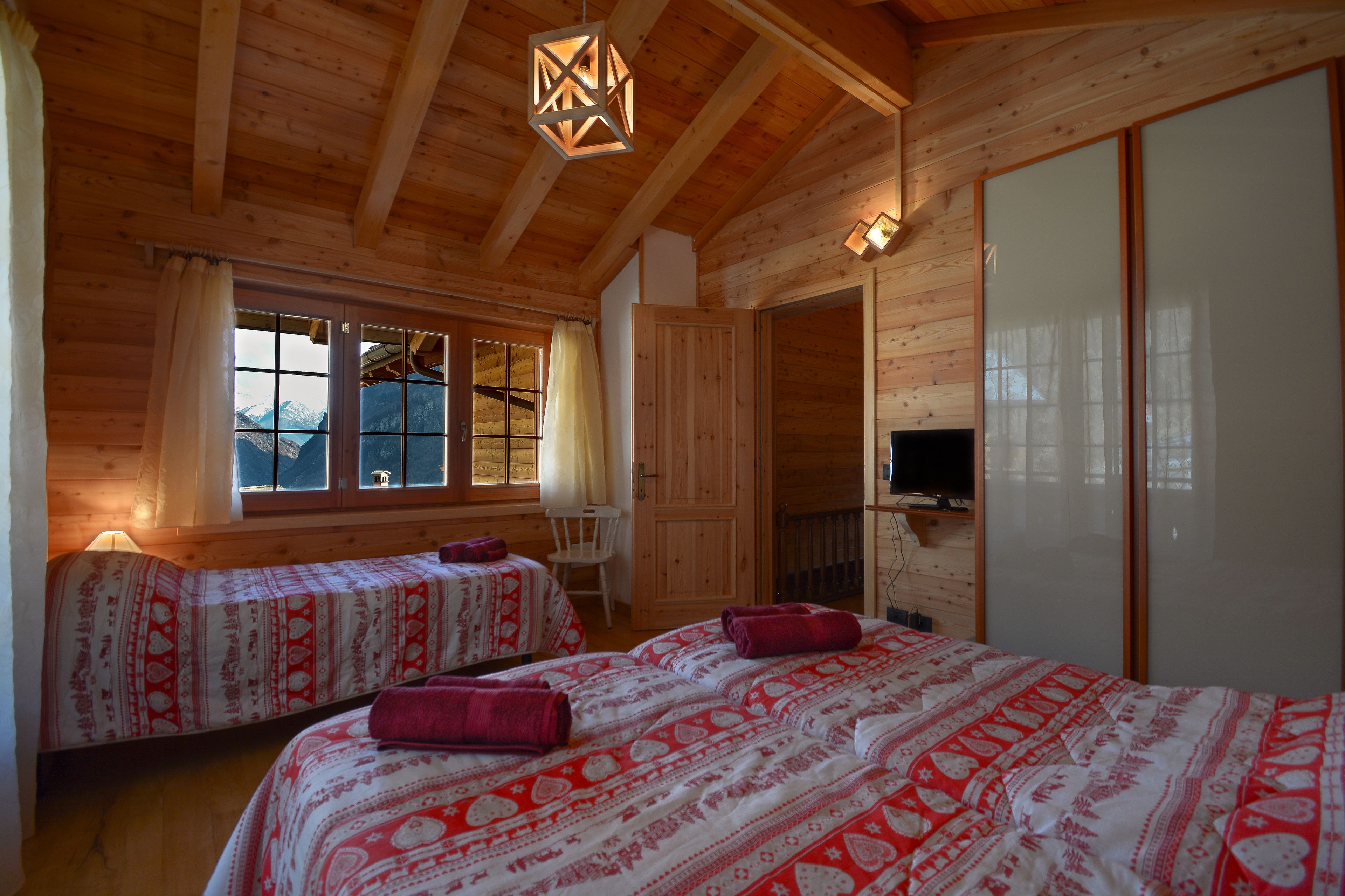 A wooden cabin room with two beds, a TV, and a large window with curtains.