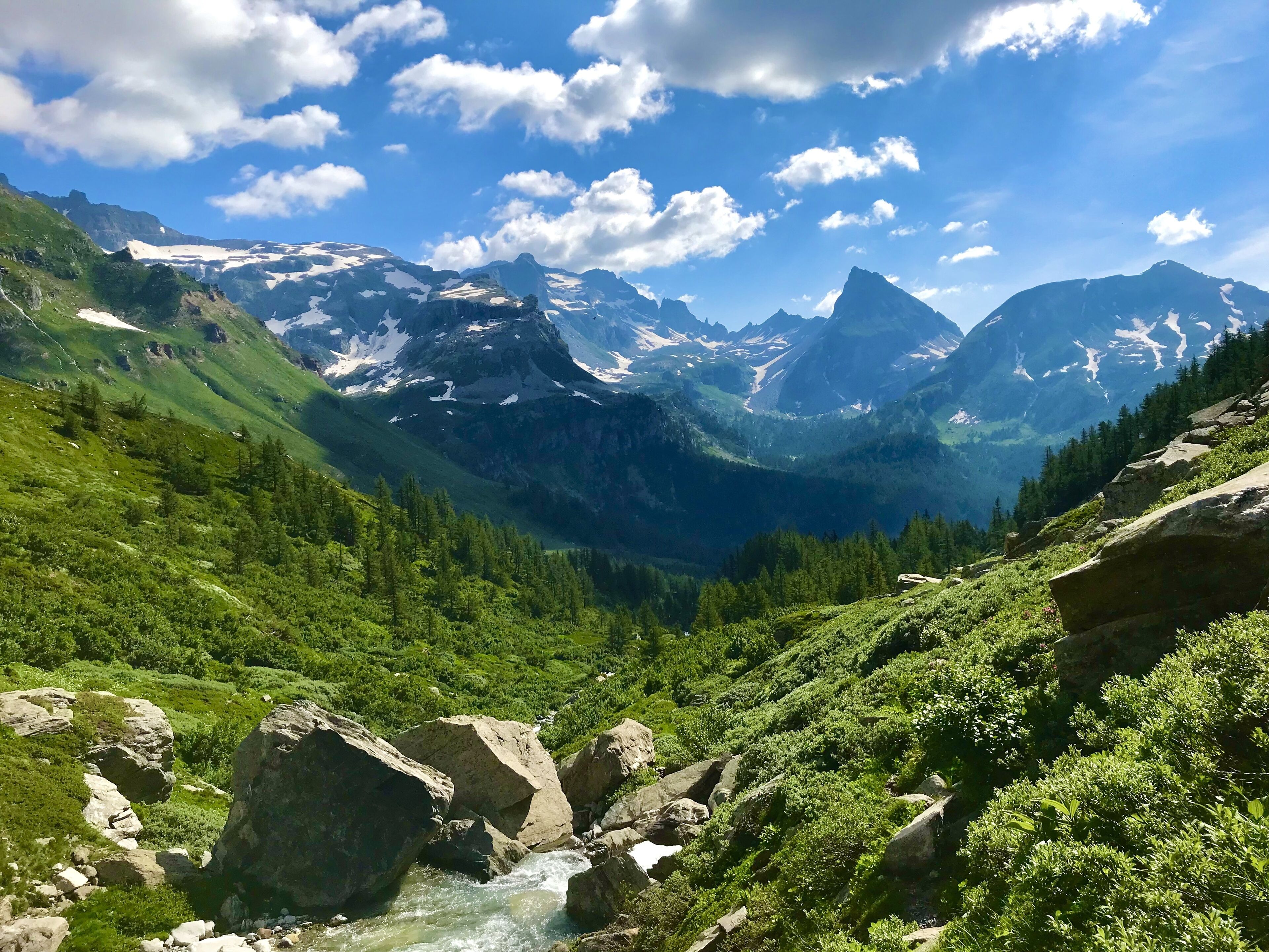 Paisaje montañoso con un río que serpentea por un valle, rodeado de colinas verdes y terreno rocoso.
