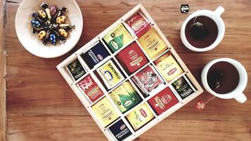 A wooden table with a bowl of colorful candies, two cups of tea, and a tray of assorted tea bags.