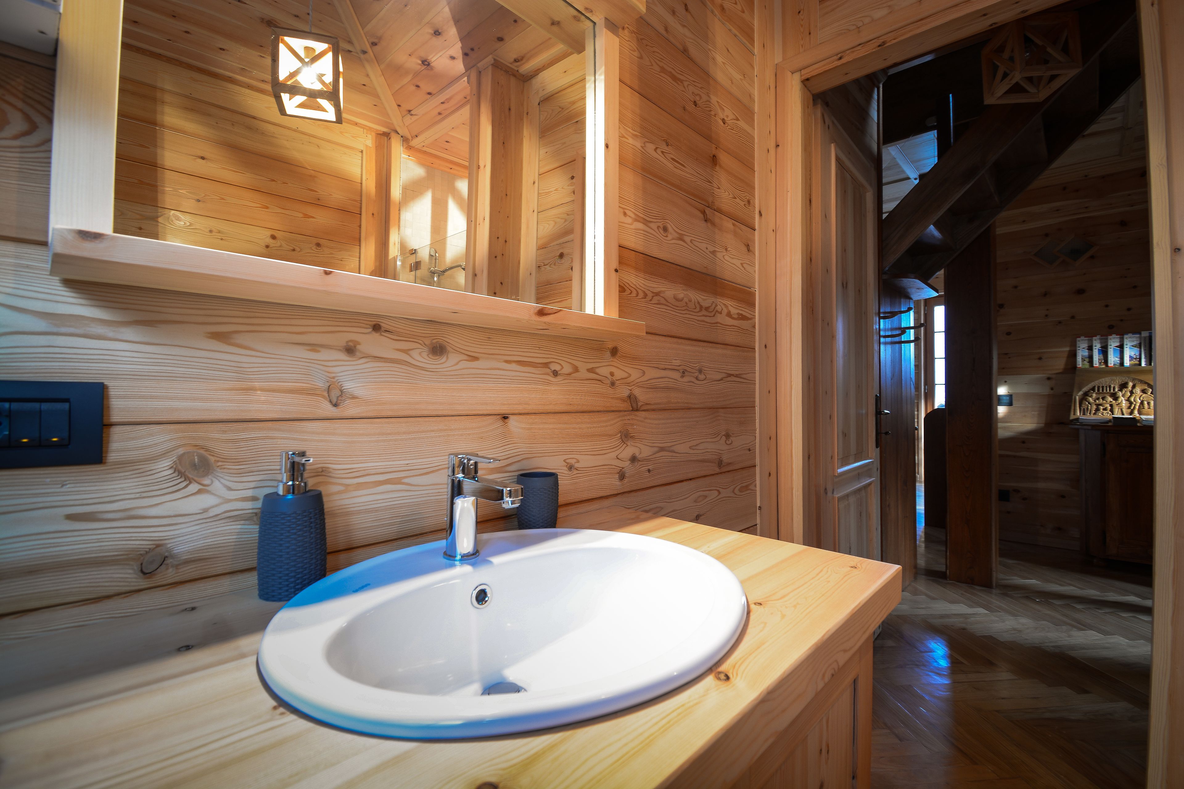 A wooden cabin interior with a round white sink, wooden walls, and a visible staircase.