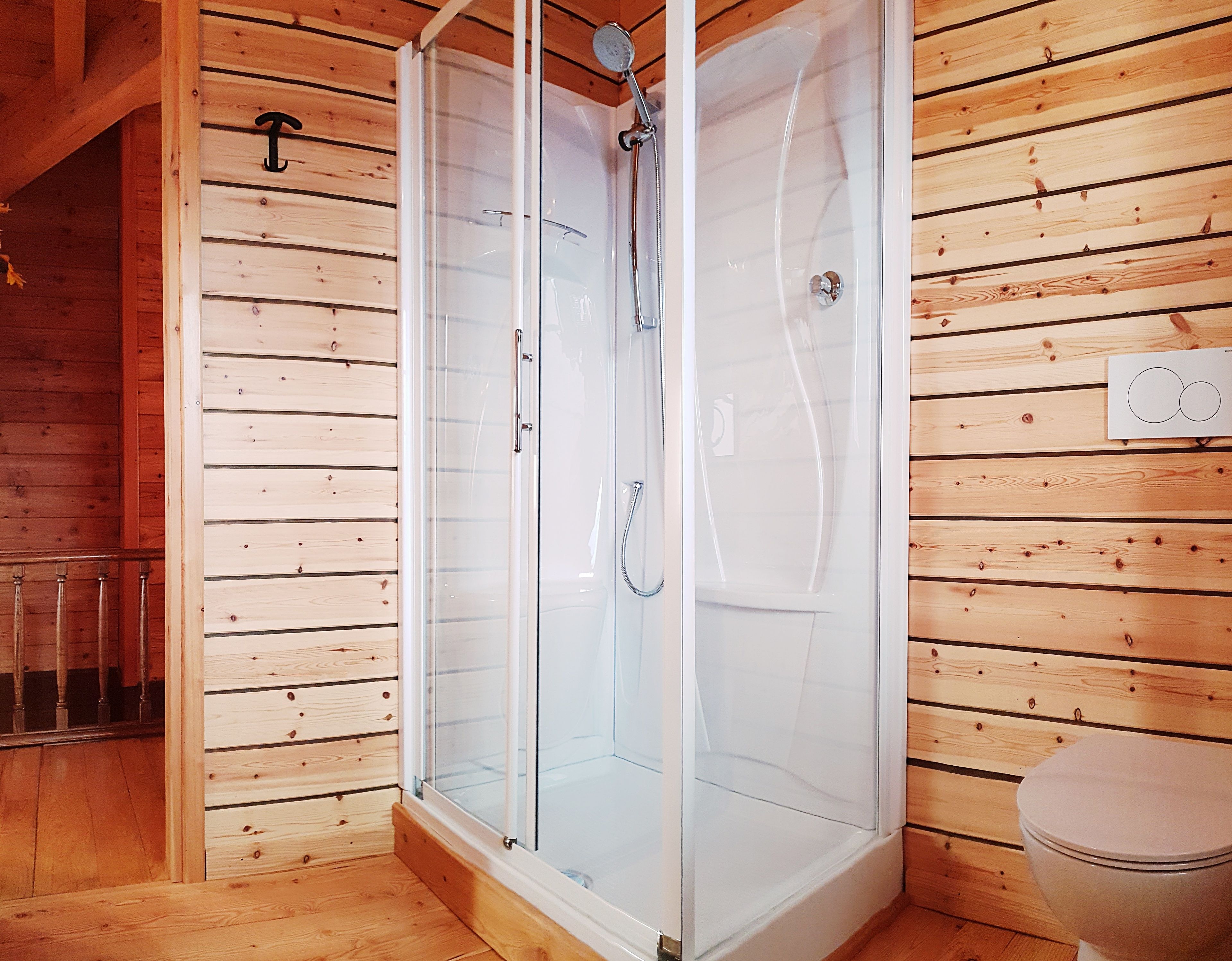 Une salle de bain rustique, avec une cabine en bois, une douche vitrée, des toilettes et un plancher en bois.