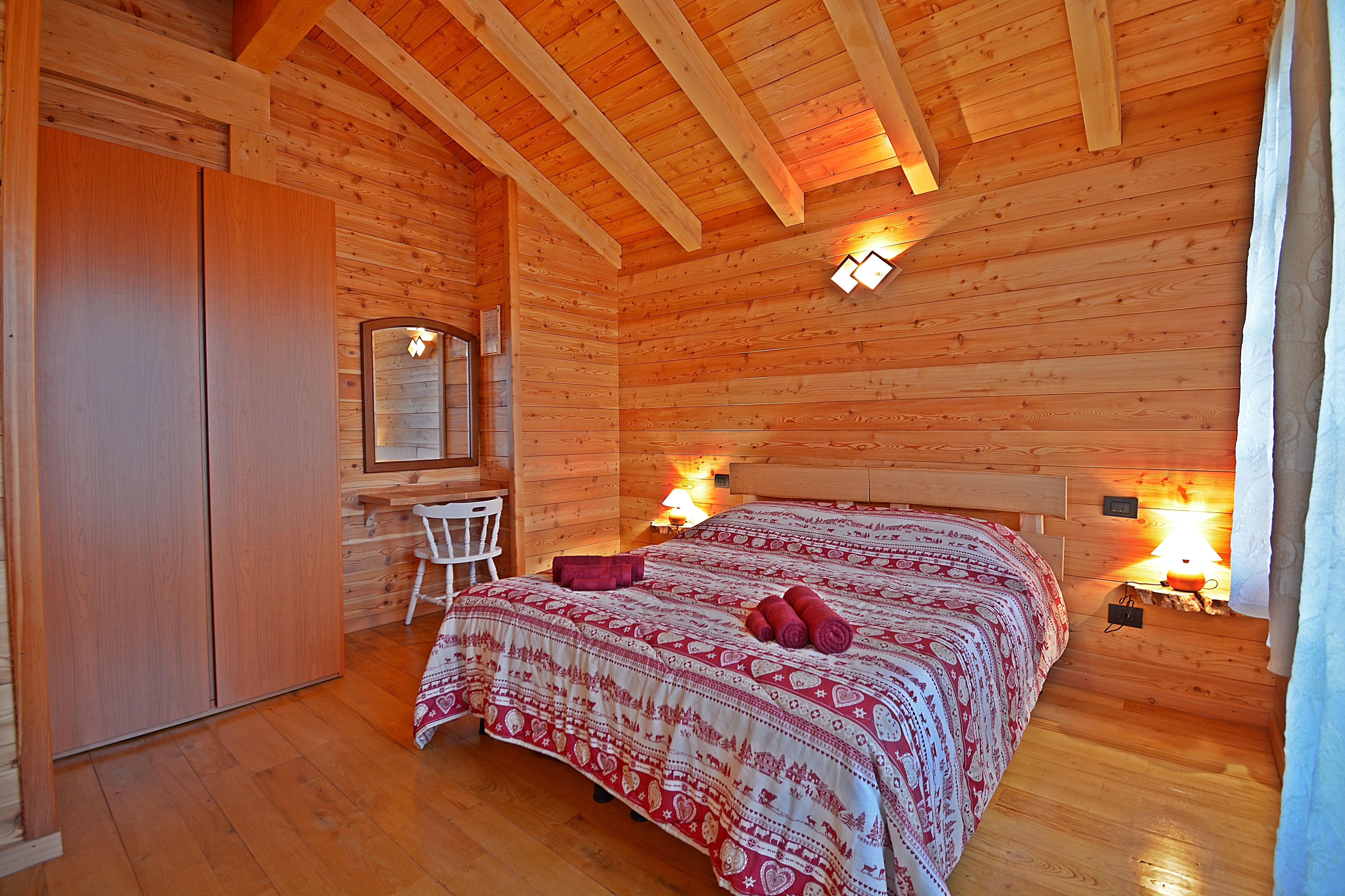 Ein Schlafzimmer einer Holzhütte mit einem Bett, Nachttischlampen, einem Sessel und einem Kleiderschrank.