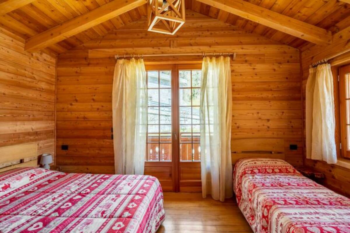 Ein Holzhütten-Zimmer mit zwei Betten, einem Vorhangfenster und einer Holzzahl.