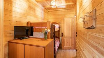 Interior de una cabaña de madera con una litera, un escritorio con televisor y una mesita con un florero.