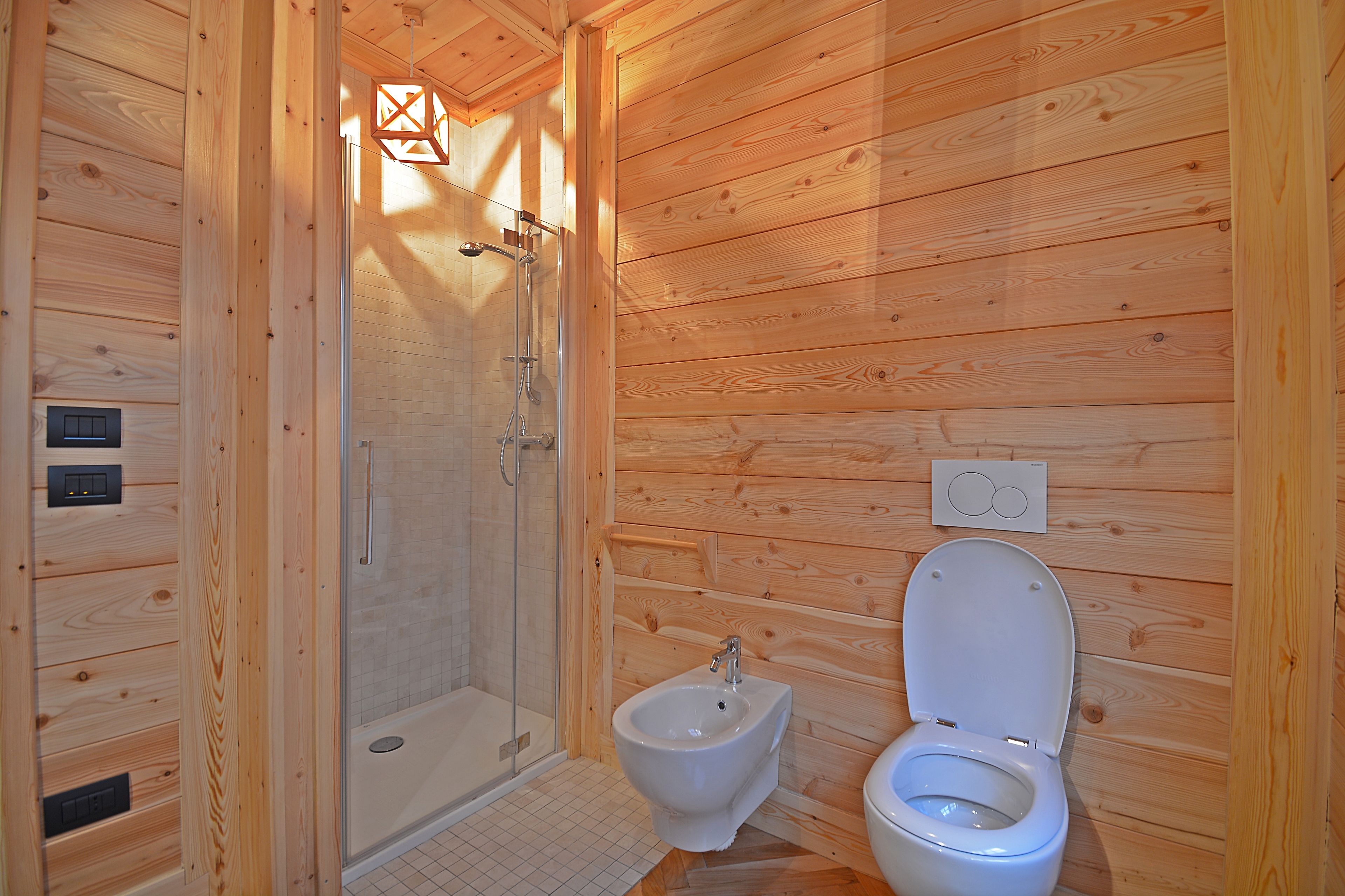 A wooden cabin bathroom with a shower, bidet, and toilet.