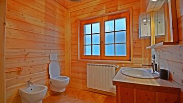 Baño de cabaña de madera con bidé, inodoro, ventana y lavabo.