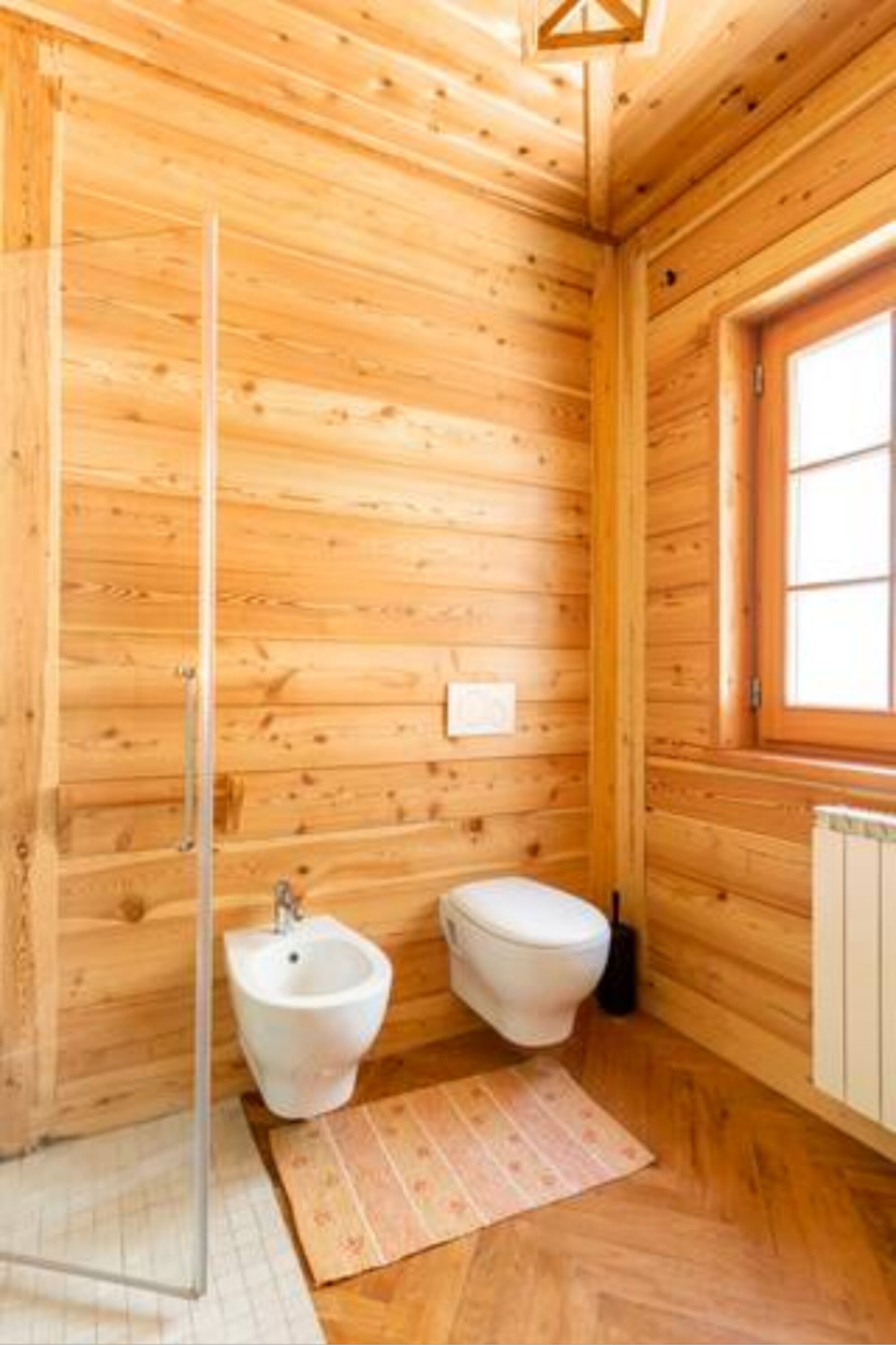 Ein Badezimmer einer Holzhütte mit Bidet, Toilette und einem Fenster.