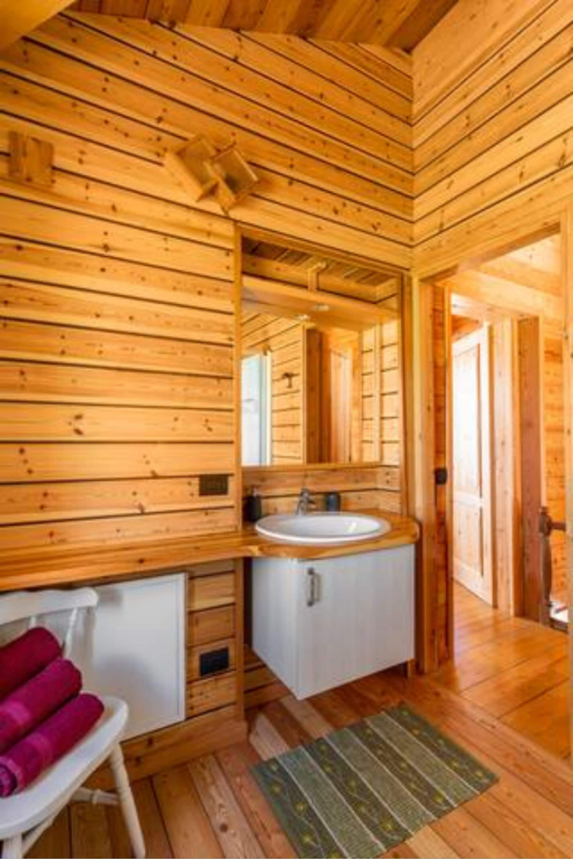 A wooden cabin interior with a wooden floor, a white sink, a mirror, and a small white cabinet.