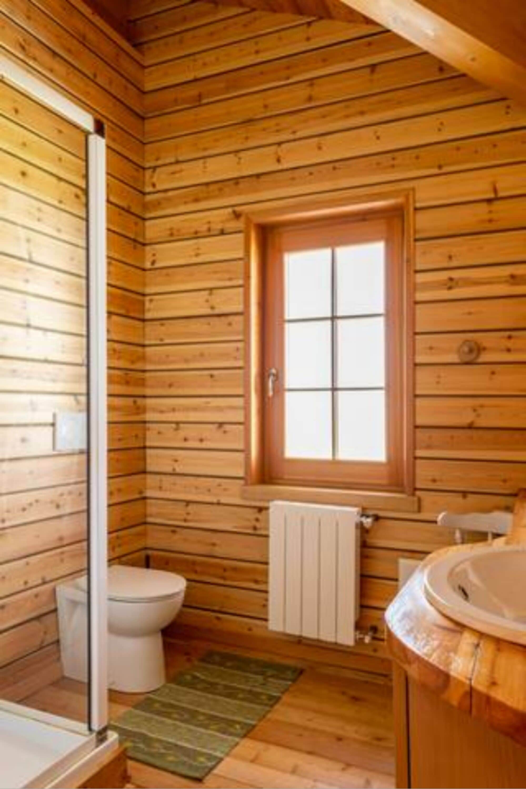 A wooden cabin bathroom with a toilet, a window, and a bathtub.