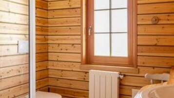 A wooden cabin bathroom with a toilet, a window, and a bathtub.