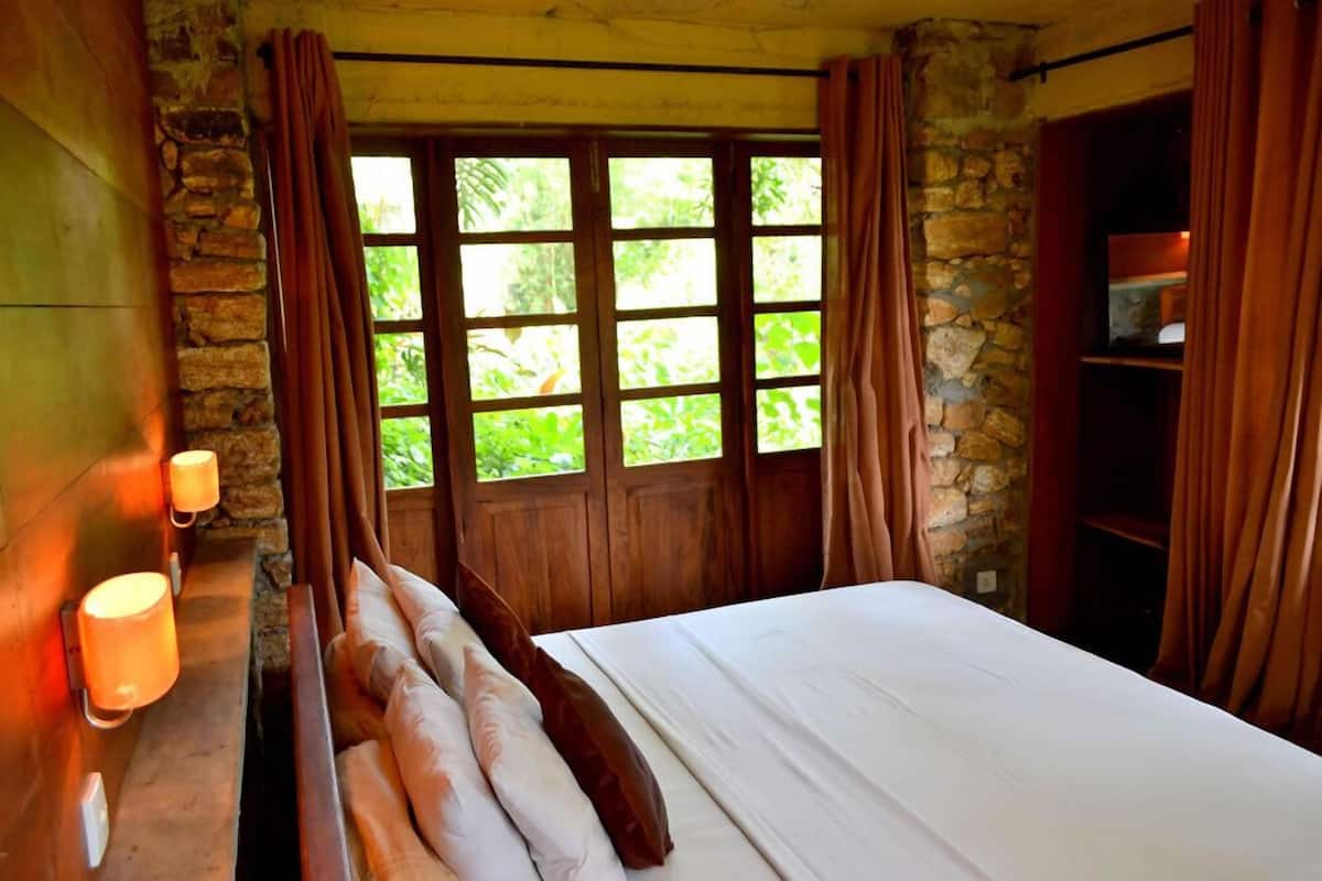 Ein Zimmer mit Bett, Steinwänden, Holzfensterrahmen und Vorhängen.