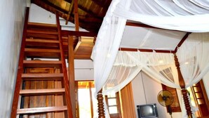 A room with a wooden staircase, a bed with a canopy, and a television. - Landa Holiday House (Imbulpe)