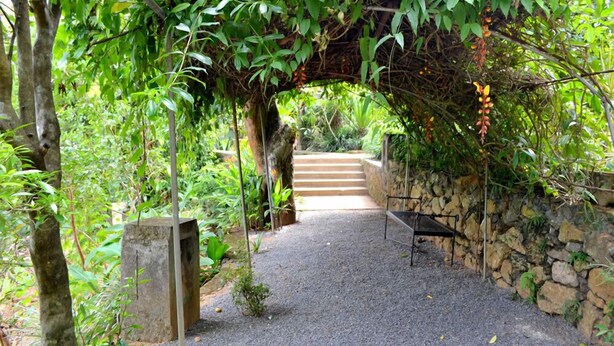 A pathway leading through a garden with a stone wall on one side and a wooden structure on the other. - Landa Holiday House (Imbulpe)