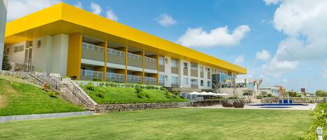 A modern building with a yellow facade, multiple balconies, and a grassy courtyard with outdoor seating.