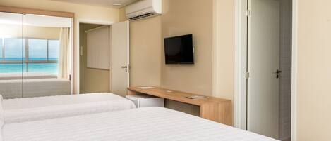 A hotel room with two beds, a TV, and a view of the ocean.