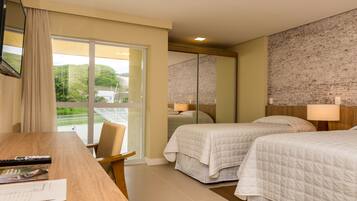 Habitación de hotel con dos camas, un escritorio con control remoto y vista a un paisaje verde a través de amplias ventanas.