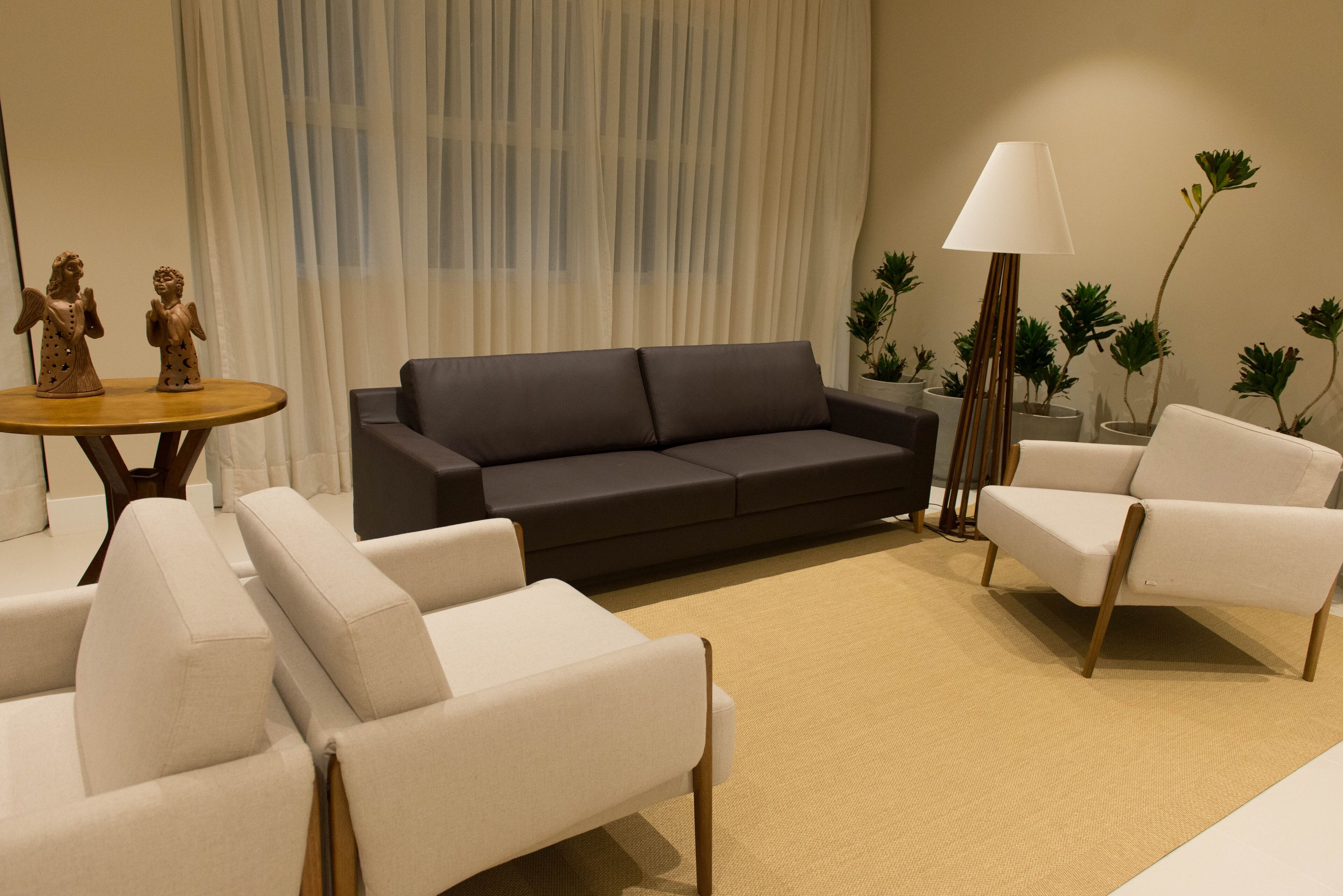 A modern living room with a dark grey sofa, white armchairs, a round wooden coffee table, and a floor lamp.