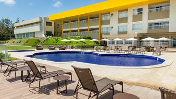 A hotel with a swimming pool, outdoor seating, and a yellow building facade.