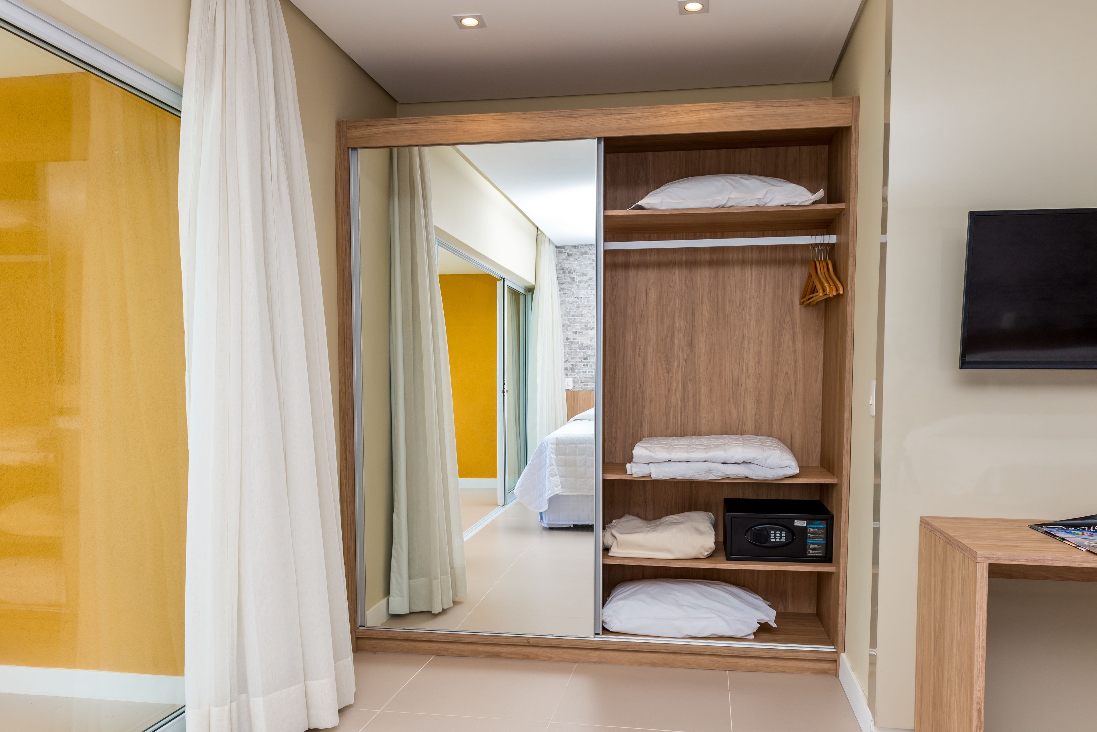 A hotel room with a wooden wardrobe, a bed, a television, and a mirror.