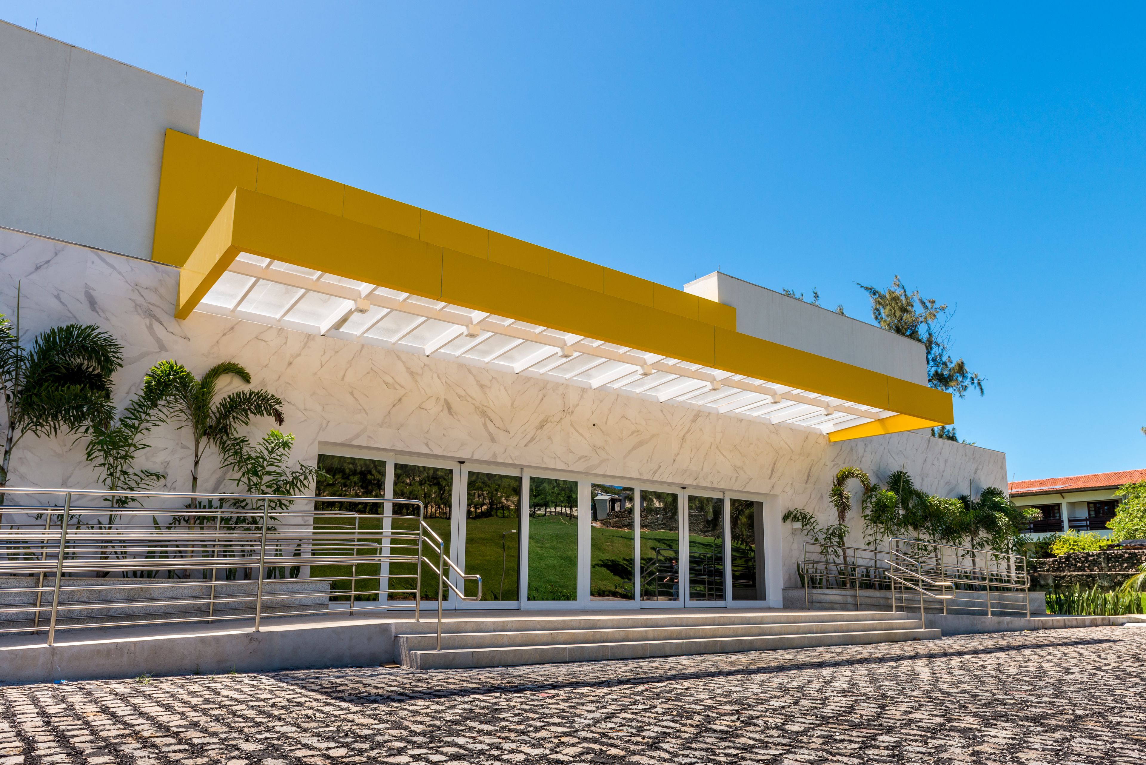 Un edificio moderno con un alero amarillo, ventanas amplias y una escalera que conduce a la entrada.
