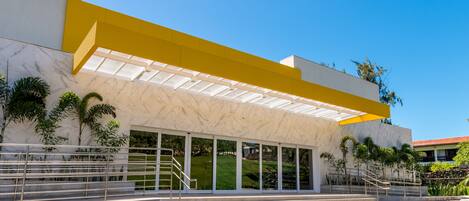 A modern building with a yellow overhang, large windows, and a staircase leading to the entrance.