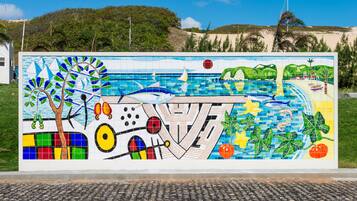 Un mural colorido con una escena de playa, que incluye un árbol, veleros y un pez.