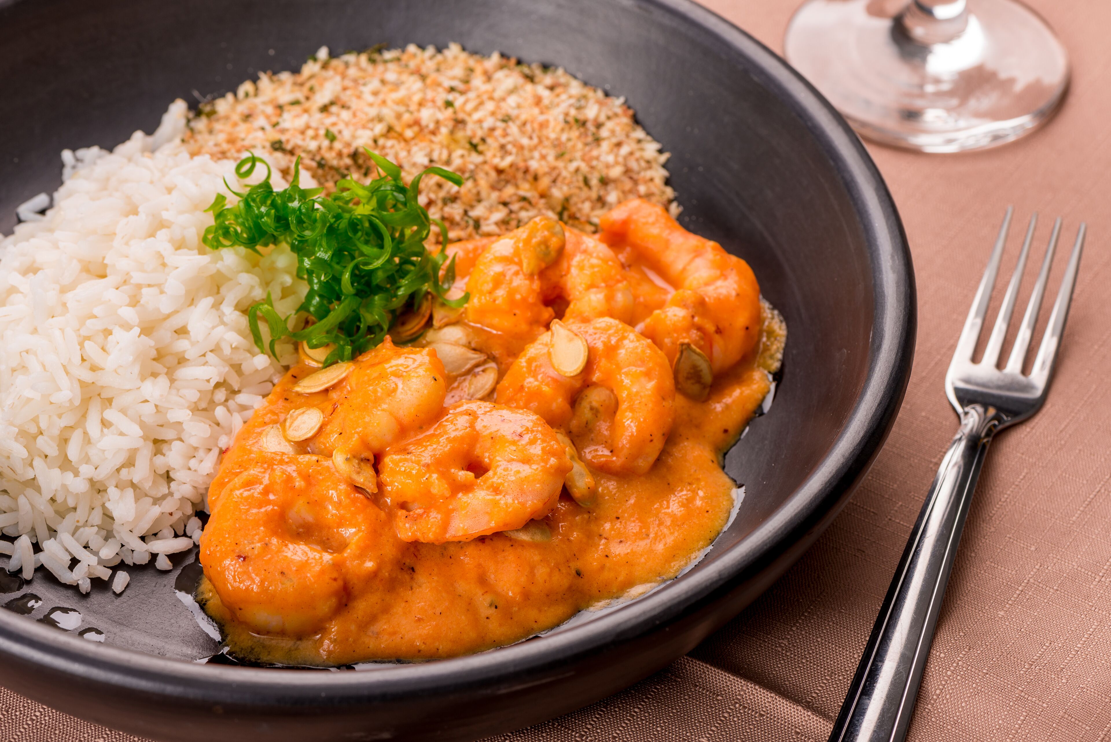 A plate of food with rice, shrimp, and a sauce, garnished with green onions and almonds.