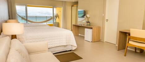 A hotel room with a bed, a desk, a chair, a small table, a lamp, a mirror, and a view of the balcony.
