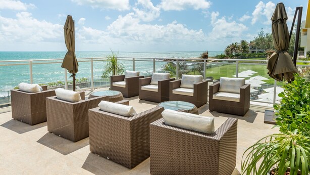 Eine Terrasse mit Korbmöbeln und Sonnenschirmen mit Blick auf einen Strand und den Ozean.