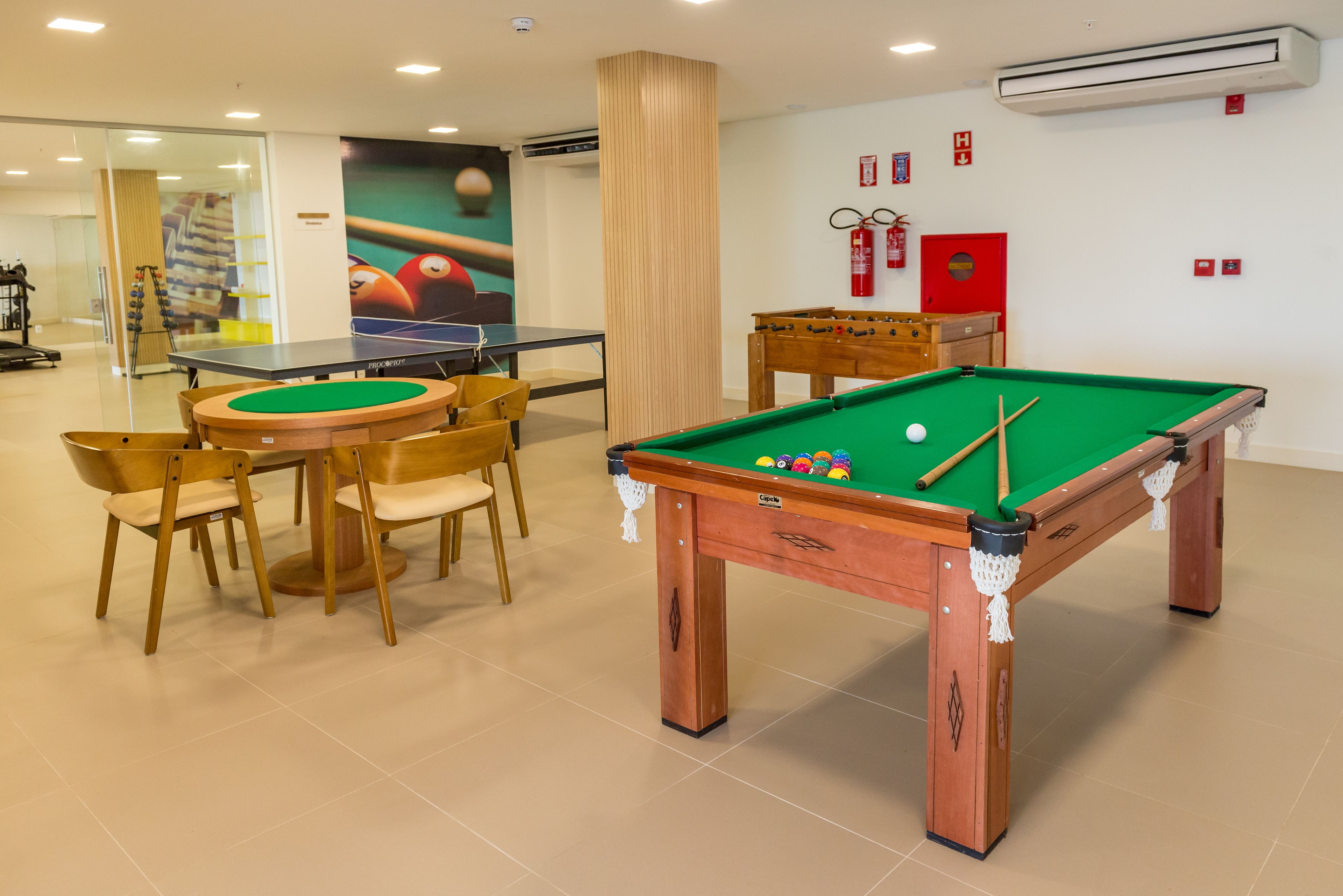 Uma sala de jogos com mesa de bilhar, mesa de futebol de mesa e mesa de pingue-pongue.