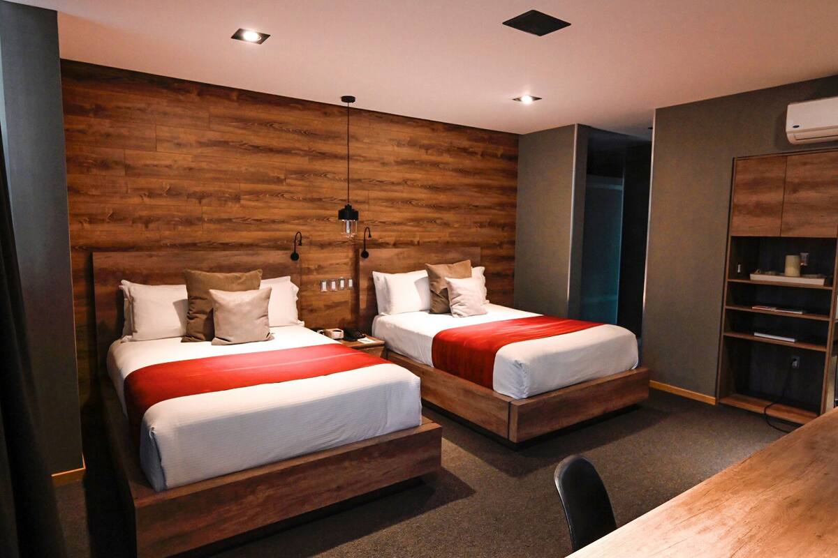 Ein modernes Hotelzimmer mit zwei Betten, Holz-Kopfteilen und einer eingebauten Bücherreolen.