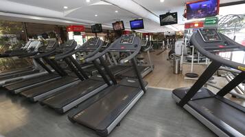 Un gimnasio con cintas de correr, equipo de ejercicio y una pantalla de televisión que muestra un programa.