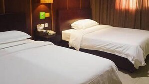 Ein Hotelzimmer mit zwei Betten, einer Hängelampe und einem Nachttisch mit Telefon und einem grünen Schild.