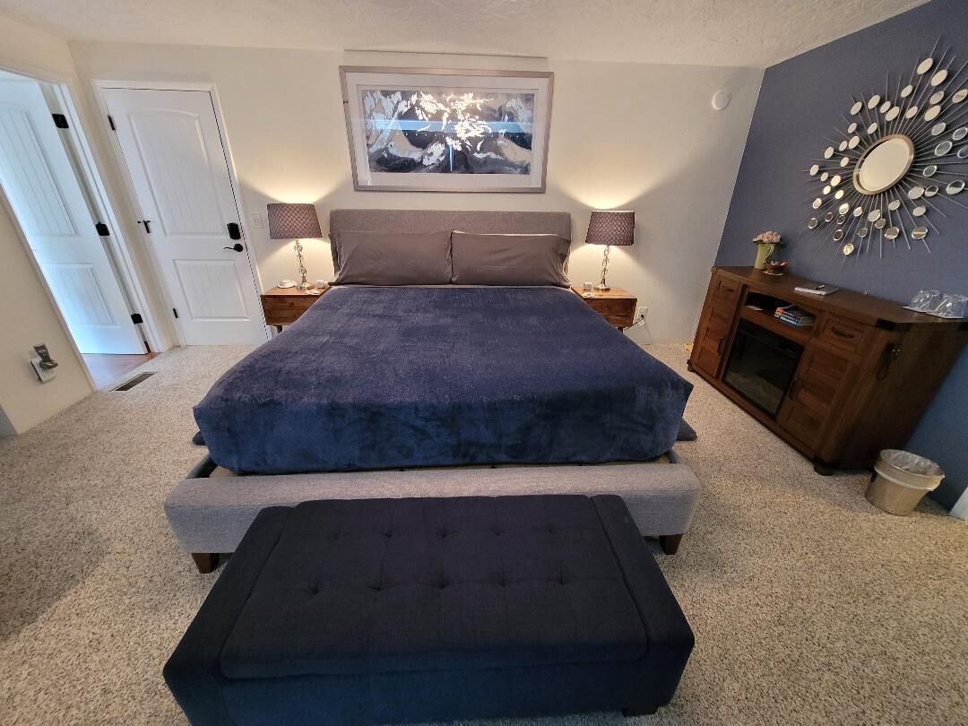Un dormitorio con una cama grande, una mesita de noche con lámparas, un aparador y un espejo montado en la pared.